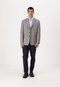 Grå rutete blazer med notched lapels, ensfarget, tre knapper, i kombinasjon med en lyseblå skjorte og marineblå bukser. Svarte sko.