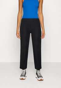 Calças pretas de cintura alta com ajuste reto e textura canelada, combinadas com uma blusa azul sem mangas e ténis pretos estampados.