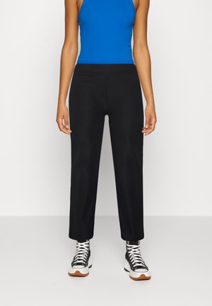 Calças pretas de cintura alta com ajuste reto e textura canelada, combinadas com uma blusa azul sem mangas e ténis pretos estampados.