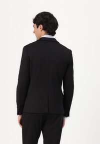 Schwarze, taillierte Sakko-Jacke mit einem einzelnen Schlitz hinten, eingefassten Revers und geknöpften Manschetten, aus glattem Stoff.