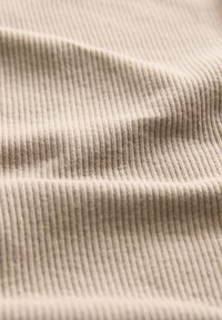 Beżowa tkanina żebrowana o miękkiej teksturze i subtelnych pionowych liniach, ukazująca fałdy i gładkie kontury materiału.