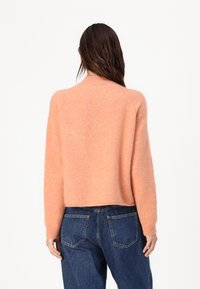 Pulover roz pufos cu decolteu rotund și mâneci lungi, cu croială scurtă, asortat cu blugi din denim albaștri, cu talie înaltă, având buzunare la spate.