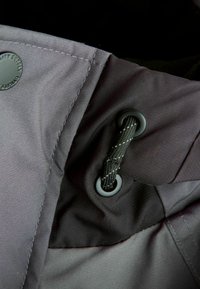 Tissu de veste imperméable gris présentant une texture lisse, des œillets et un cordon noir avec de subtils détails de couture.