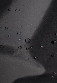 Zwart gestructureerde stof met verschillende waterdruppels op het oppervlak, die de waterdichte eigenschappen benadrukken.