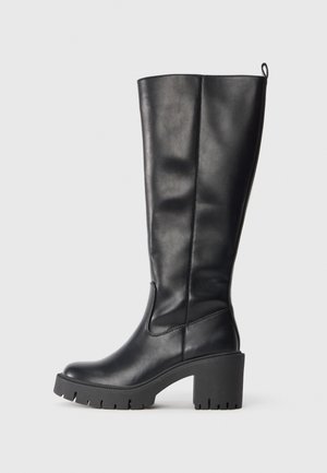 Knee-high black leather boots with a smooth texture, chunky rubber heel, and lug sole. Features a pull tab for easy wear.