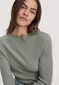 Rippstrickpullover in sanftem Grün, Rundhalsausschnitt, lange Ärmel, mit einer subtilen Textur und klassischer Passform, kombiniert mit Denim.