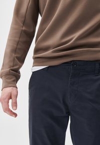 Hanorac maro cu un finisaj texturat și mâneci lungi, asociat cu pantaloni chino bleumarin cu închidere prin buton și buzunare laterale.