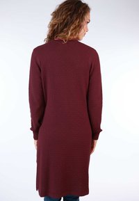 Long maroon cardigan with a textured pattern, round neckline, and long sleeves. Sides feature slits for ease of movement.