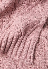 Rožinės spalvos megztinis audinys su tekstūruotu raštu ir riboto pynimo detalėmis. Siūlai yra storas ir minkštas, suteikiantys jaukų vaizdą.
