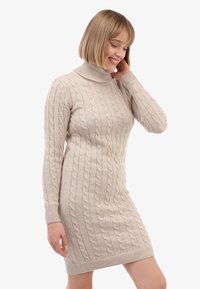 Beeži nööriga kootud kleit, millel on vale kõrge kaelus, soonilised mansetid ja serv. Kujundatud istuva silueti ja tekstuuriga mustriga.