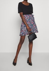 Haut noir à manches courtes assorti d'une jupe imprimée florale en bleu, rose et blanc. Tient un petit sac à main noir texturé. Talons noirs.