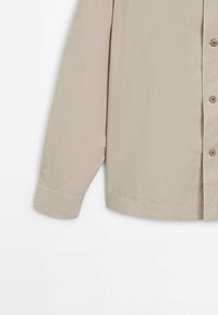 Camicia beige a maniche lunghe con colletto, realizzata in tessuto liscio. Presenta un orlo dritto e una chiusura a bottoni sul davanti.