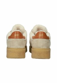 Wildlederschuhe in Cremefarbe mit einem flauschigen weißen Innenfutter, braunen Lederakzenten an der Ferse und einer strukturierten Gummisohle. Sichtbares goldfarbenes Branding.