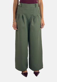 Groene wijde broek met plooien, hoge taille, gladde stof en zijzakken; gecombineerd met puntige schoenen.