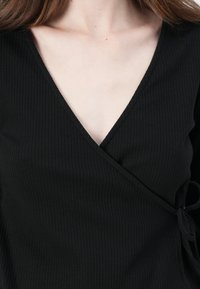 Černý žebrovaný top s volným zavinovacím stylem a hlubokým výstřihem do V, s detailem na zavázání na boku a hladkou strukturou.
