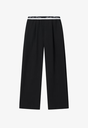 Schwarze, weit geschnittene Hose mit elastischem Bund und weißem "Another Cotton" Schriftzug als Markenzeichen.