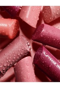 Rouges à lèvres dans différentes teintes de rose et de baies, avec une texture glossy et des gouttelettes d'eau s'accrochant à la surface, disposés de manière rapprochée.