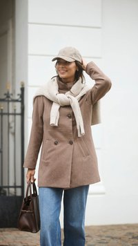Brown wool blend coat with double-breasted closure, paired with a cream knit scarf. Light blue wide-leg jeans and a small brown handbag.