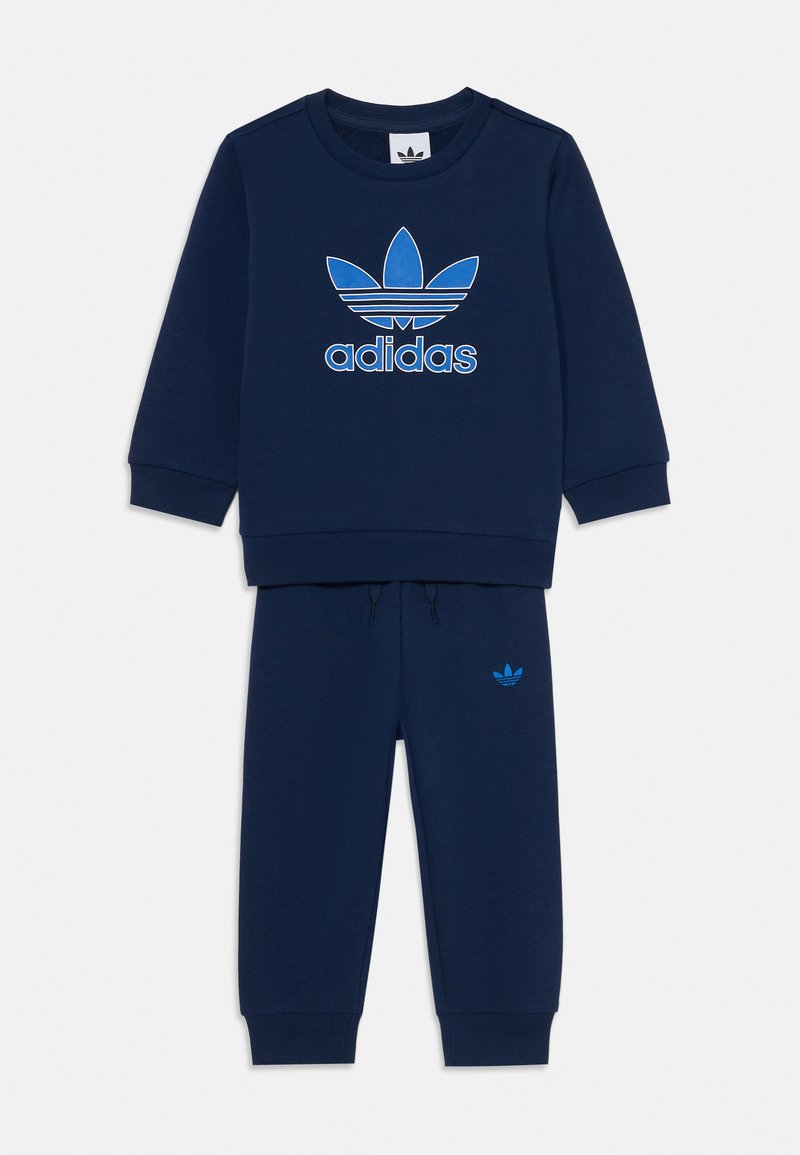 Sötétkék pulóver és nadrág szett puha anyagból. A pulóverén egy nagy kék Adidas logó található; a nadrágon egy kis logó látható a deréknál.