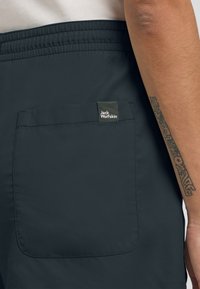 Dunkelnavy Shorts aus glattem Stoff mit einem elastischen Bund und einer Innentasche, die mit einem Jack Wolfskin-Logo versehen ist.