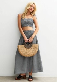 Black and white gingham two-piece set featuring a cropped top with adjustable straps and a long skirt. Woven straw handbag with round handle.