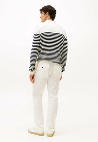 Maglione a righe blu navy e bianco, texture a maglia, con pantaloni bianchi e sneakers bianche. Mostra un design casual e dal taglio rilassato.