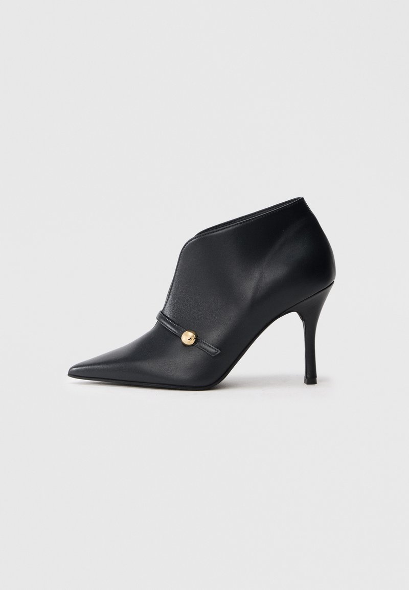 Μαύρα δερμάτινα μποτάκια αστραγάλου με μυτερές μύτες, ψηλές στιλέτο τακούνια και διακοσμητικό χρυσό στοιχείο σε λουράκι.