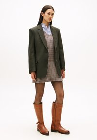 Brune lærstøvler til knæene, grønn stripet blazer, kjole med hundetannmønster og blå stripete skjorte med krage. Glatte teksturer.