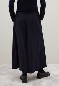 Marineblauwe wijde broek met een elastische tailleband, gemaakt van een gladde stof, gecombineerd met zwarte plateauschoenen. Eenvoudig, minimalistisch ontwerp.