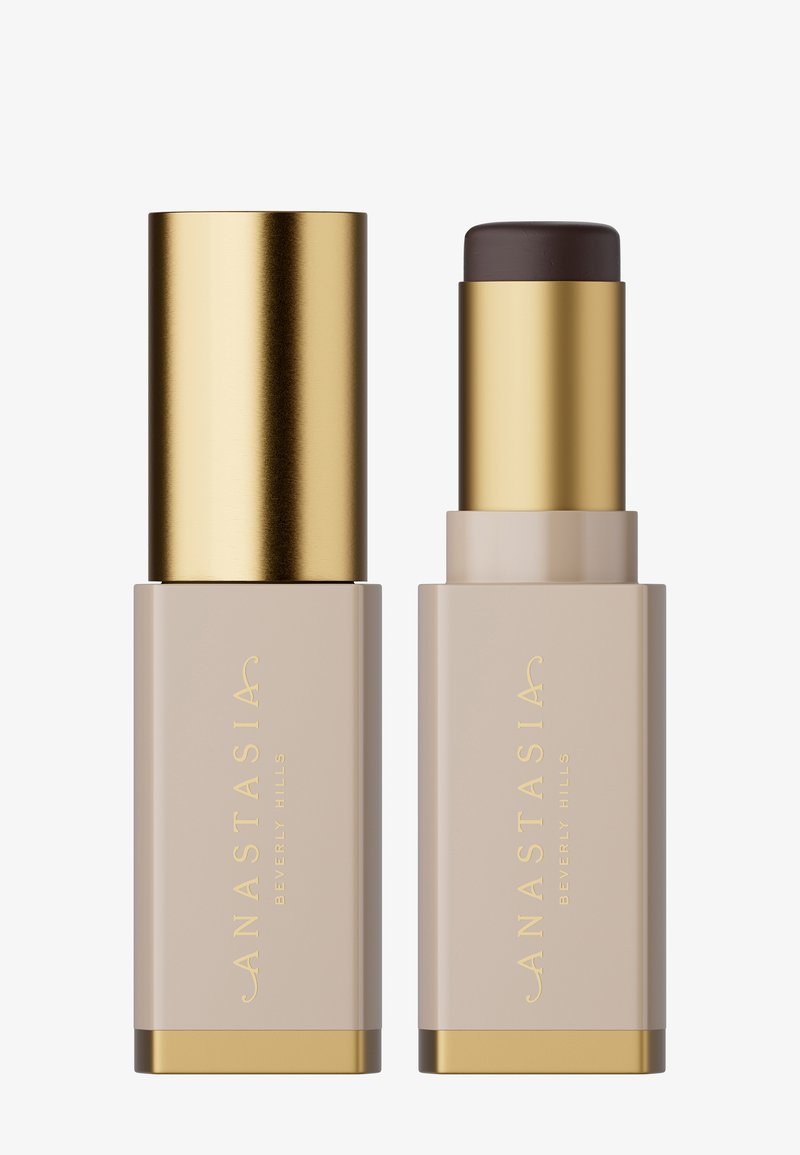 Kremowy podkład w sztyfcie w beżowej obudowie z złotymi akcentami. Gładka tekstura, cylindryczny kształt. Nakrętka nad ciemniejszym sztyftem, wyraźnie oznaczona.