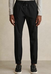 Black jogger pants with an elastic waistband, front pockets, and fitted cuffs. Smooth fabric with a slight sheen and ankle zippers.