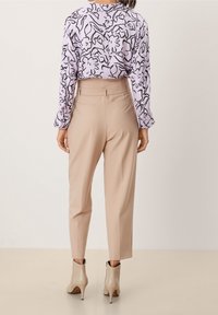 Ljuslila blus med svart blommönster, matchad med beige tapered byxor och nude högklackade ankelstövlar. Släta texturer genomgående.