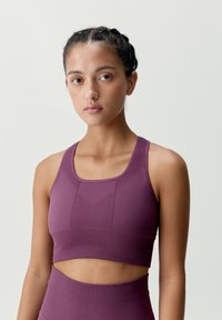 Lila atletisk crop top med ribbat mönster, geometriska designdetaljer och breda axelband. Den har en åtsittande silhuett med en utskärning.