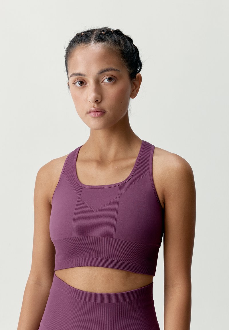 Lila atletisk crop top med ribbat mönster, geometriska designdetaljer och breda axelband. Den har en åtsittande silhuett med en utskärning.