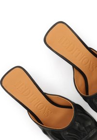 Paire de sandales noires en cuir sans lacets avec semelles intérieures carrées beige embossées du nom de la marque, vues de dessus sur fond blanc.