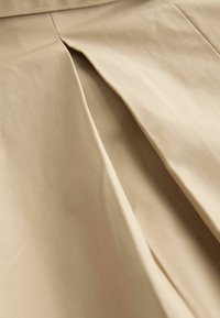 Beige fabric with a smooth texture, featuring pleats and crisp stitching details. The design highlights soft draping and flowing lines.