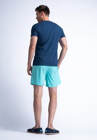 Camiseta azul marino, pantalones cortos turquesa claros, estilo casual. Zapatos de tela oscura con suela de cuerda. Diseño minimalista, corte simple y ajustado.