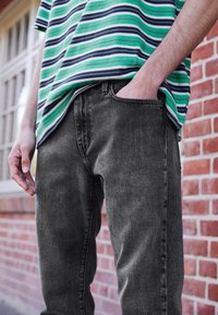 Zwarte denim jeans met een rechte snit, voorzien van een vijf-pocket ontwerp en subtiele textuur, gecombineerd met een groen gestreept T-shirt met korte mouwen.