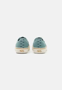 Teal canvas sneakers med mönstrad baksida, beige gummisula och märkesdetaljer. Minimalistisk design och låg profil.