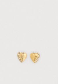 Χρυσά σκουλαρίκια σε σχήμα καρδιάς με κρυσταλλικές λεπτομέρειες κατά μήκος της μίας άκρης και με την ανάγλυφη επωνυμία "GUESS" σε κάθε σκουλαρίκι, με λείο μεταλλικό φινίρισμα.