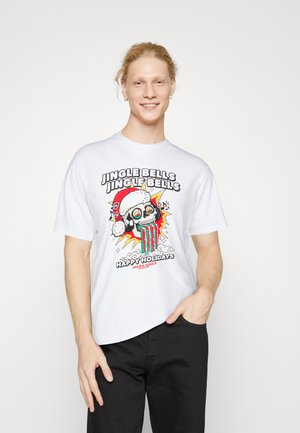 T-shirt en coton blanc ornée d'un design graphique coloré représentant un crâne portant un chapeau de Noël, avec du texte et des détails colorés dégoulinants. Pantalons noirs portés.
