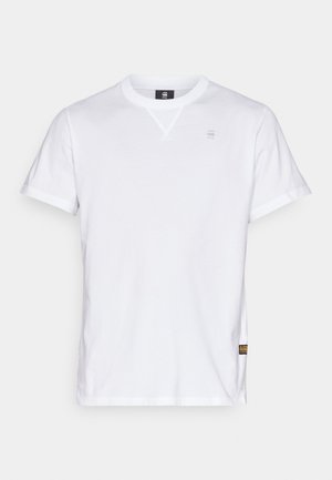 Bela bombažna majica s kratkimi rokavi, okroglo izrezom in majhnim logotipom na prsih. Ima stransko etiketko za identifikacijo blagovne znamke.