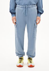 Helle blaue Cargo-Hosen mit elastischem Bund und Bündchen, ausgestattet mit seitlichen Taschen. Kombiniert mit leuchtend gelben und roten Sportschuhen.