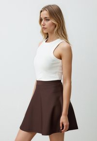Weißes ärmelloses Oberteil, kombiniert mit einem knielangen braunen ausgestellten Rock. Der Stoff wirkt glatt mit einem dezenten Schimmer. Einfaches Design ohne Muster.