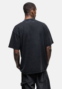 Overmaatse zwarte katoenen T-shirt met een ronde hals, korte mouwen en minimaal detail aan de achterkant. Gekocht in combinatie met bijpassende donkere spijkerbroek.