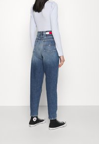 Högmidjade blå denimjeans med smalnande ben, blekt tvätt, två bakfickor och märkesmidja, ihop med svarta hög-top sneakers.