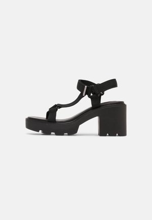 Schwarze Absatzsandalen mit einer klobigen, strukturierten Plattformsohle, ausgestattet mit verstellbaren Stoffriemen und einem Zehenring-Design.