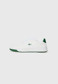 Witte sneaker van leer met een groene hiel en zool. Voorzien van witte veters en een klein groen logo aan de zijkant. Minimalistisch ontwerp.
