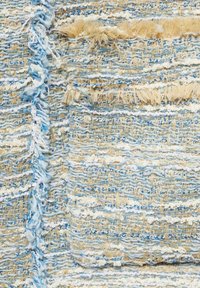 Gros plan d’un tissu tissé texturé avec des fils bleus, beiges et blancs présentant des détails de fil lâche et effiloché.