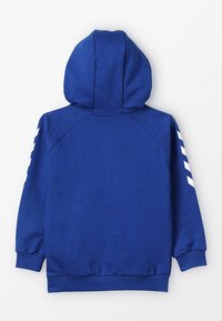 Felpa blu in cotone con maniche lunghe, tasca anteriore e strisce bianche diagonali su ciascun braccio. Caratterizzata da un cappuccio con cordino.